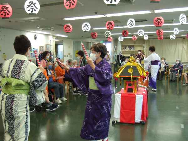 浴衣を着たボランティアさんがバチを持って踊っているところ